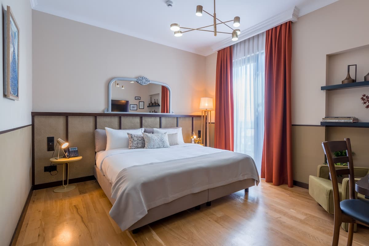 A modern hotel bedroom with a large bed, bedside lamps, a desk, and a chair.