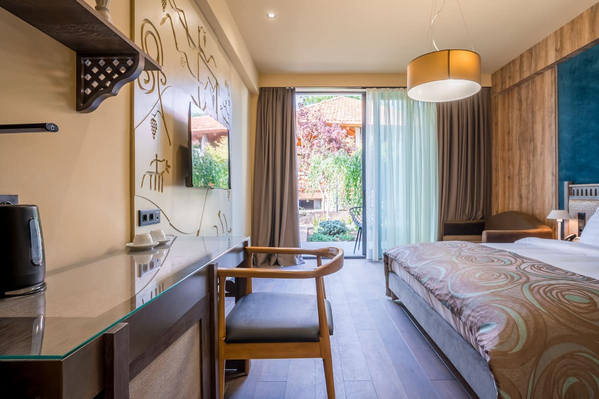 A hotel room with a bed, a desk with a chair, a television, and a view of the outdoors.