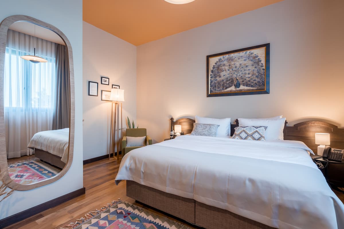 A hotel room with a large bed, a mirror, a peacock painting, and a telephone on the nightstand.