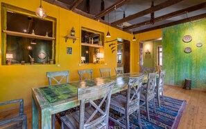 A dining area with a long table and chairs, yellow walls, and wooden beams.