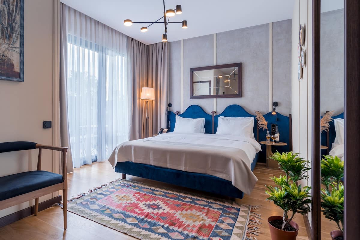 A modern hotel room with a large bed, a desk, a chair, and a large window with curtains.