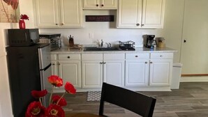 A compact kitchen with white cabinets, a black refrigerator, and a coffee maker. - Ell's Room (Harkers Island)