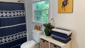 A bathroom with a shower curtain, toilet, window, and a poster on the wall. - Ell's Room (Harkers Island)