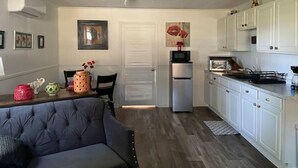A compact living space with a kitchenette, a dining area with a sofa, and a door leading to another room. - Ell's Room (Harkers Island)