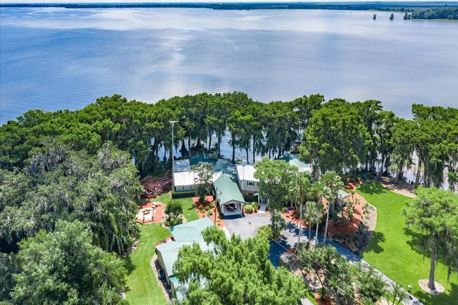 An aerial view of a lakeside property with a house surrounded by dense trees and a clear view of the lake.