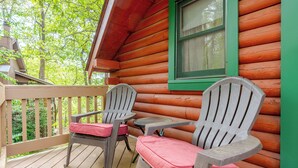 Una cabaña de madera con dos sillas Adirondack y una pequeña mesa en el porche.