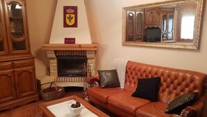 A living room with a fireplace, leather sofa, wooden cabinet, and a mirror. - Casa Rural Rincón de Ayllón (ayllon)