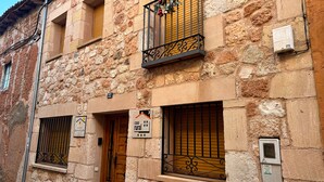 A rustic stone building with a wooden door, barred windows, and a balcony with decorative elements. - Casa Rural Rincón de Ayllón (ayllon)