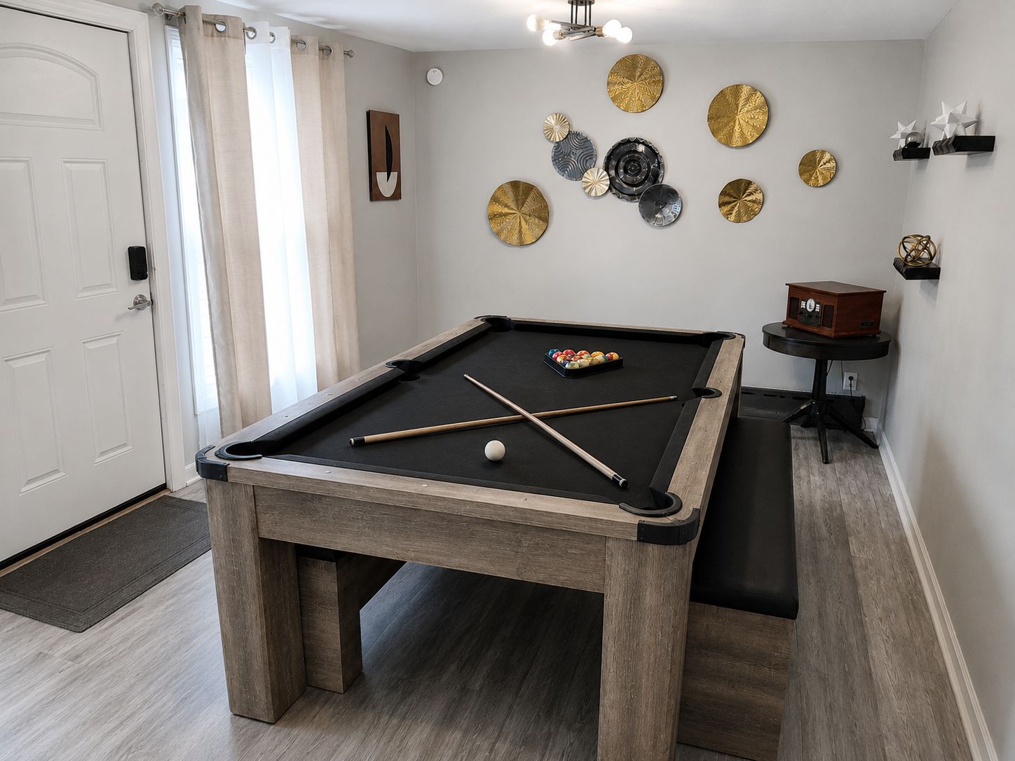 Una mesa de billar con tacos y bolas, un despertador de radio, platos decorativos en la pared y una puerta con cortinas.