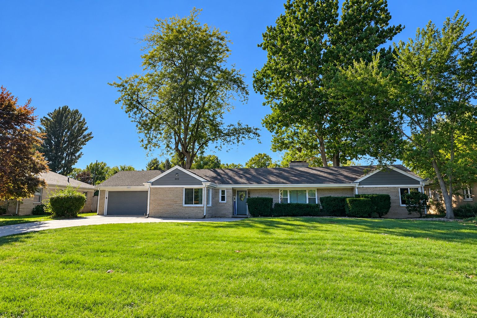 A single-story house with a garage, a front lawn, and mature trees.