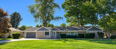 A single-story house with a garage, a front lawn, and mature trees.