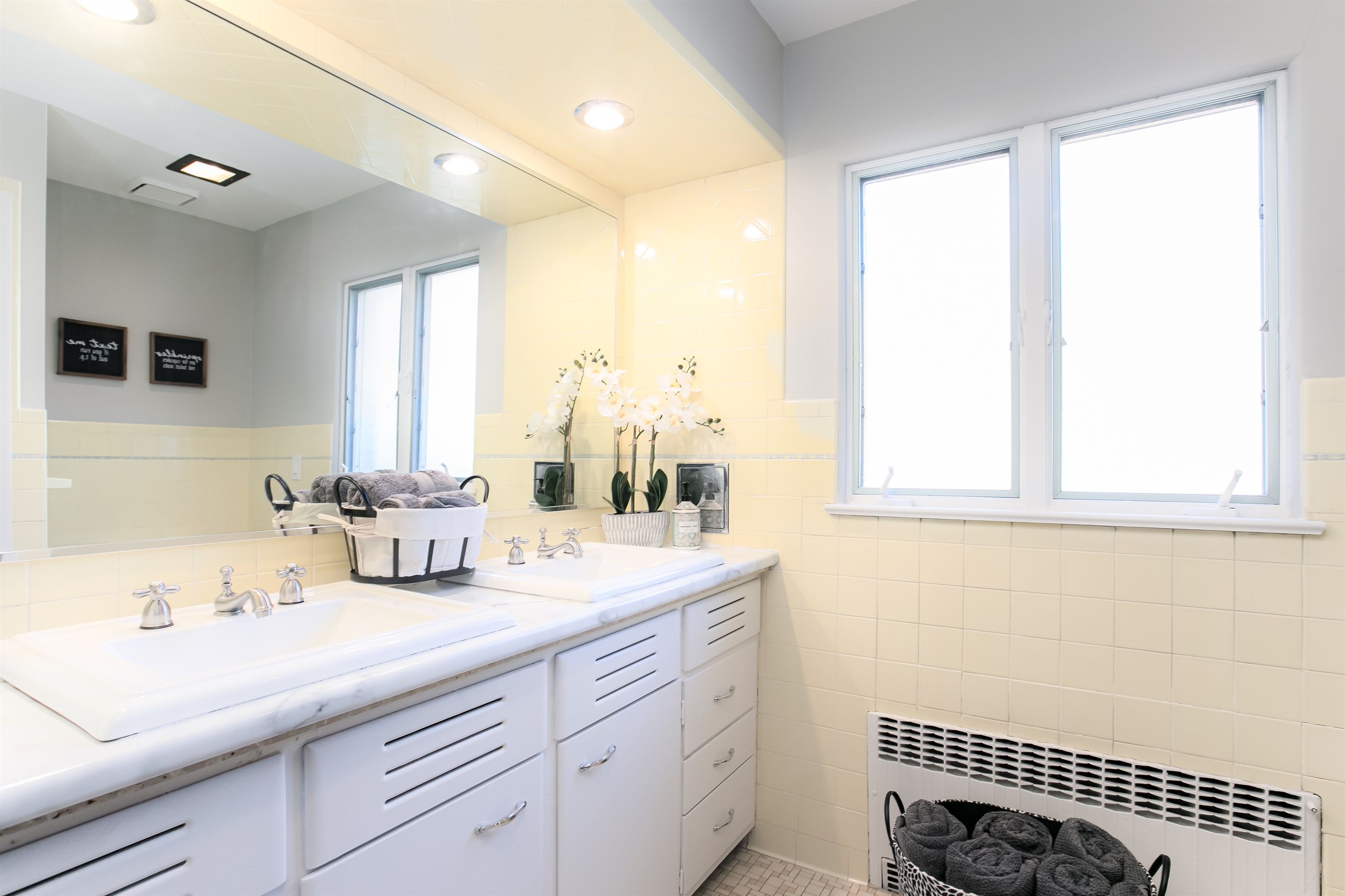 Une salle de bain moderne avec un grand miroir, deux lavabos, un porte-serviettes et une fenêtre.