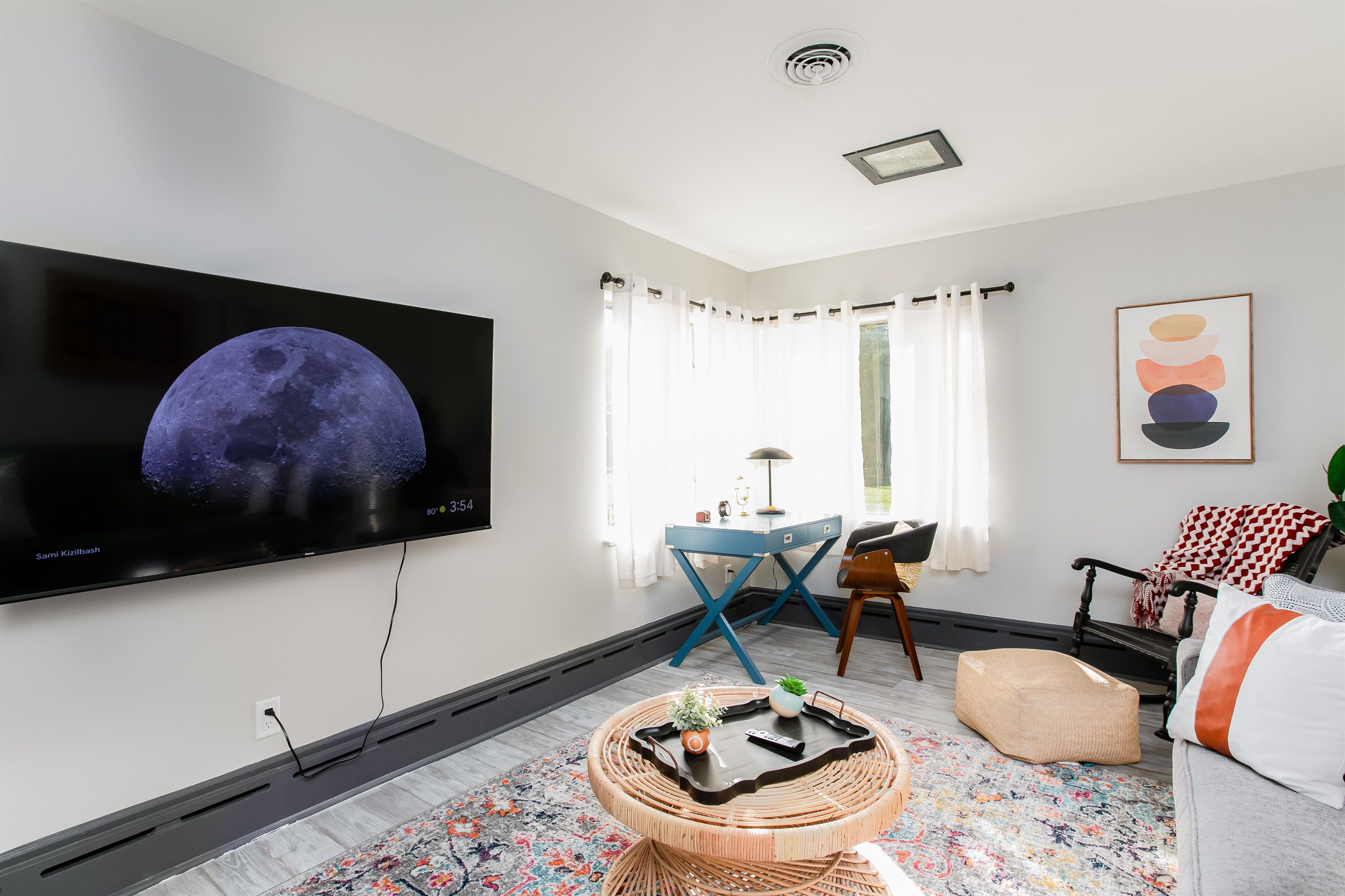 Una sala de estar moderna con un televisor de pantalla plana, un escritorio azul, una mesa de centro de mimbre y una alfombra estampada.
