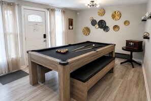 A pool table with balls and cues, a wooden bench, and decorative plates on the wall.