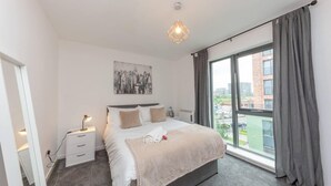 Une chambre d’hôtel moderne avec un grand lit, une table de chevet, une commode, une fenêtre avec des rideaux et une vue sur la ville.