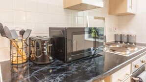 Une cuisine avec un plan de travail noir, un grille-pain, un four à micro-ondes et une machine à café. Il y a des placards au-dessus du plan de travail et une fenêtre donnant sur un espace verdoyant.
