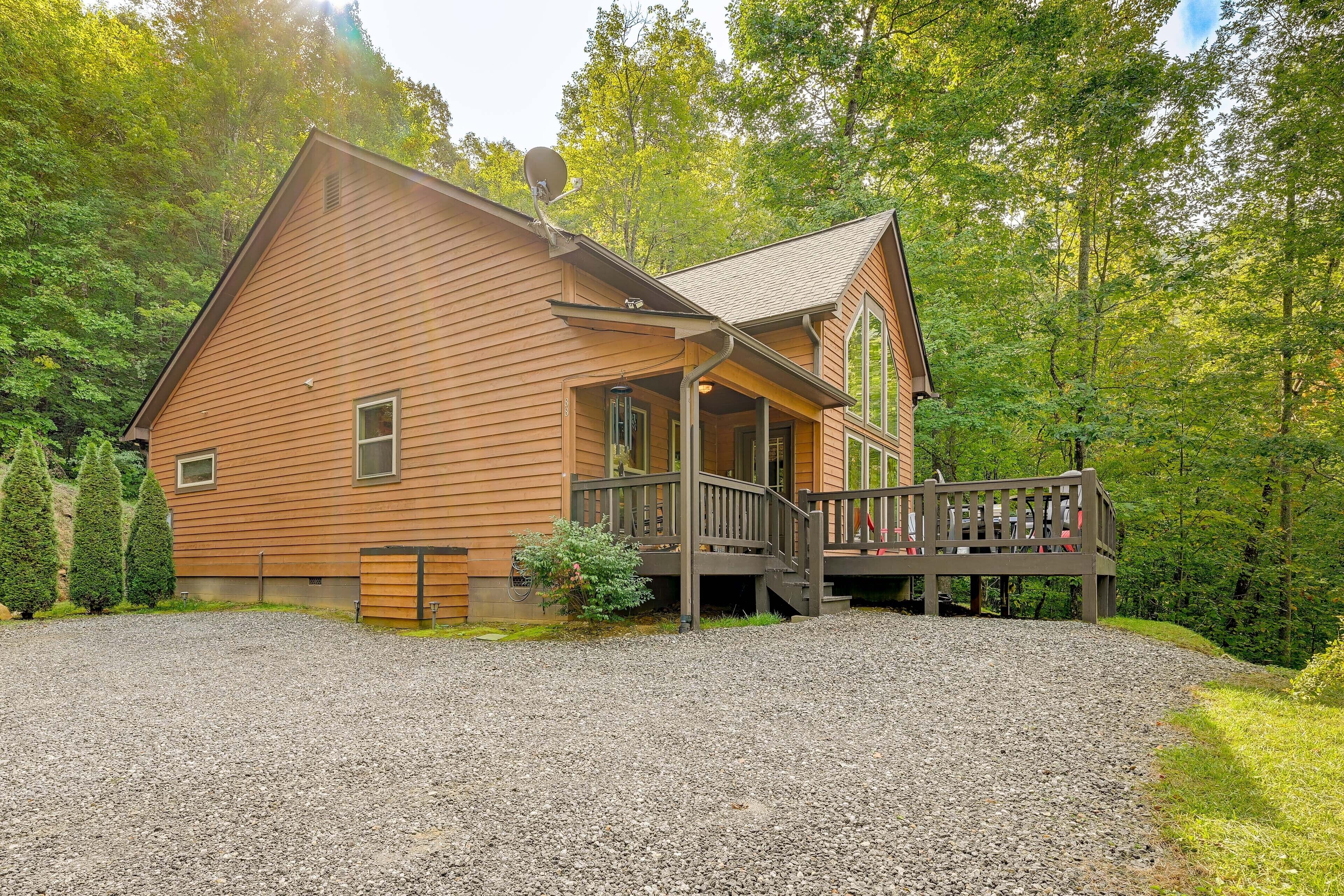 A wooden cabin with a porch, gravel driveway, and surrounded by trees.