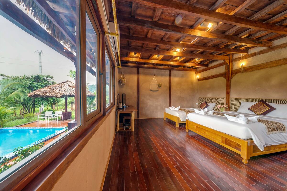 Ein Schlafzimmer mit Holzboden, einem großen Fenster mit Blick auf einen Pool und einem Bett mit weißer Bettwäsche.