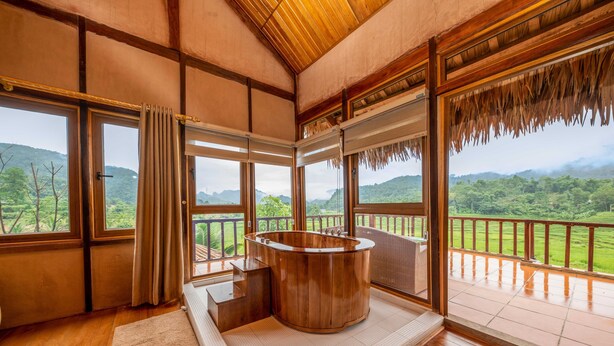 Un intérieur en bois agrémenté d’un bain à remous, de grandes fenêtres et d’une vue sur un paysage verdoyant.