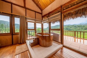 Un intérieur en bois agrémenté d’un bain à remous, de grandes fenêtres et d’une vue sur un paysage verdoyant.
