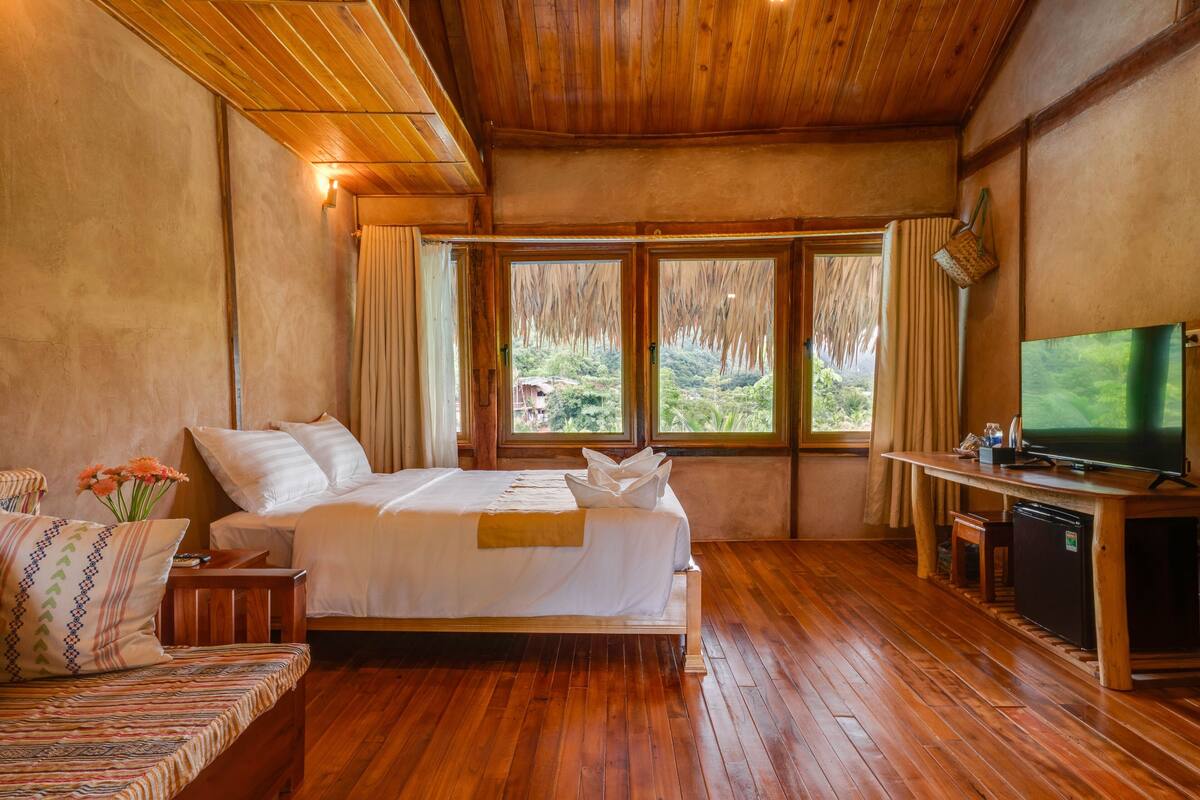 Ein Schlafzimmer mit einem hölzernen Bett, einem Fernseher und Blick auf Grün.