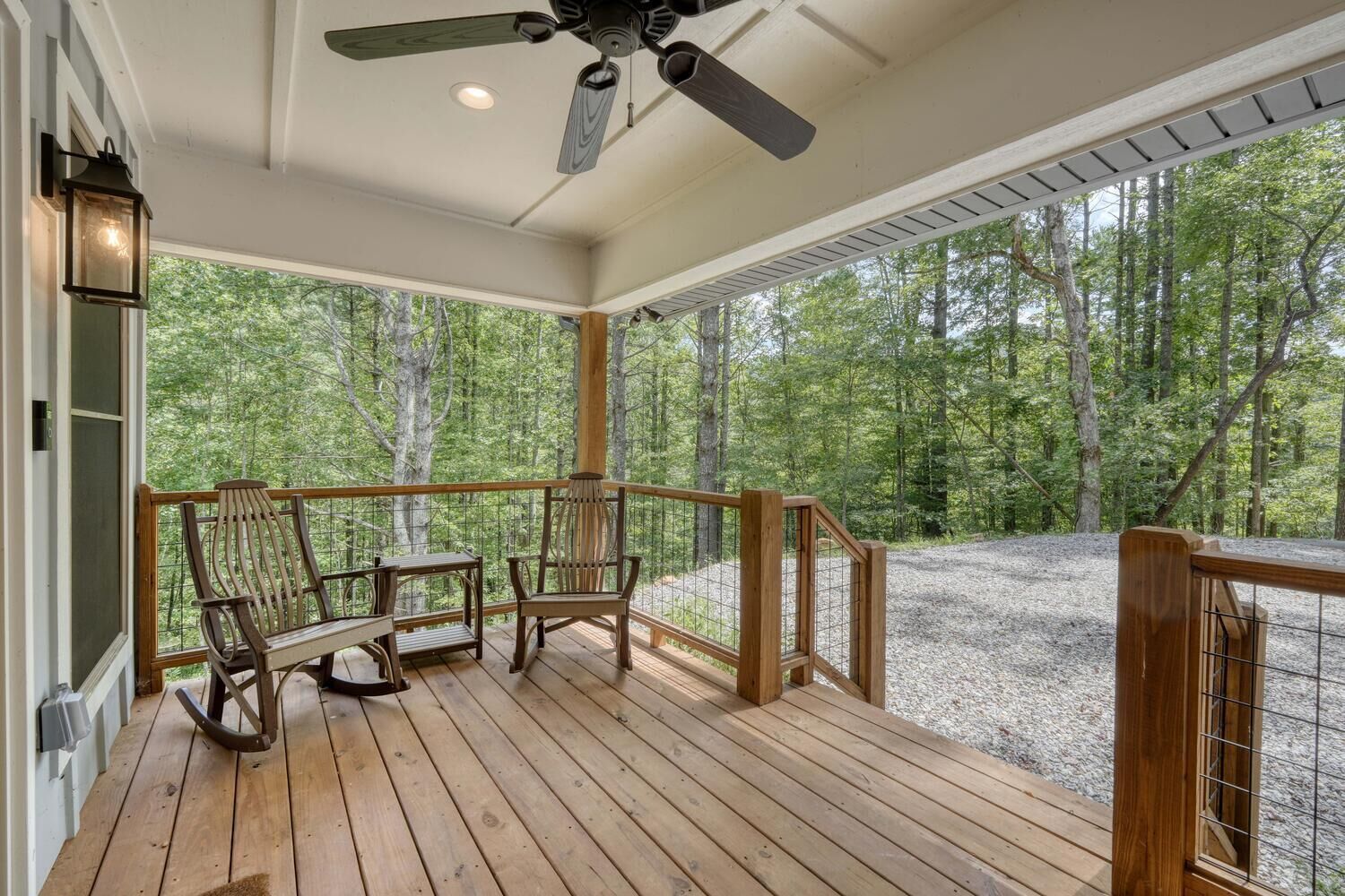 A wooden deck with a ceiling fan, two rocking chairs, and a view of a forest.