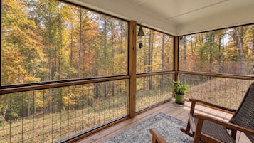 A room with large windows, a wooden floor, and a seating area with a rug.