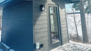 Une petite cabane en bois sombre, avec une cheminée, une fenêtre et une porte.