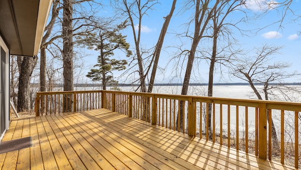 Une terrasse en bois dotée d’une rambarde, qui offre une vue sur une étendue d’eau et des arbres.