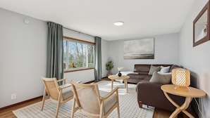 Un salon moderne avec un canapé, deux fauteuils en bois, une petite table et une lampe.