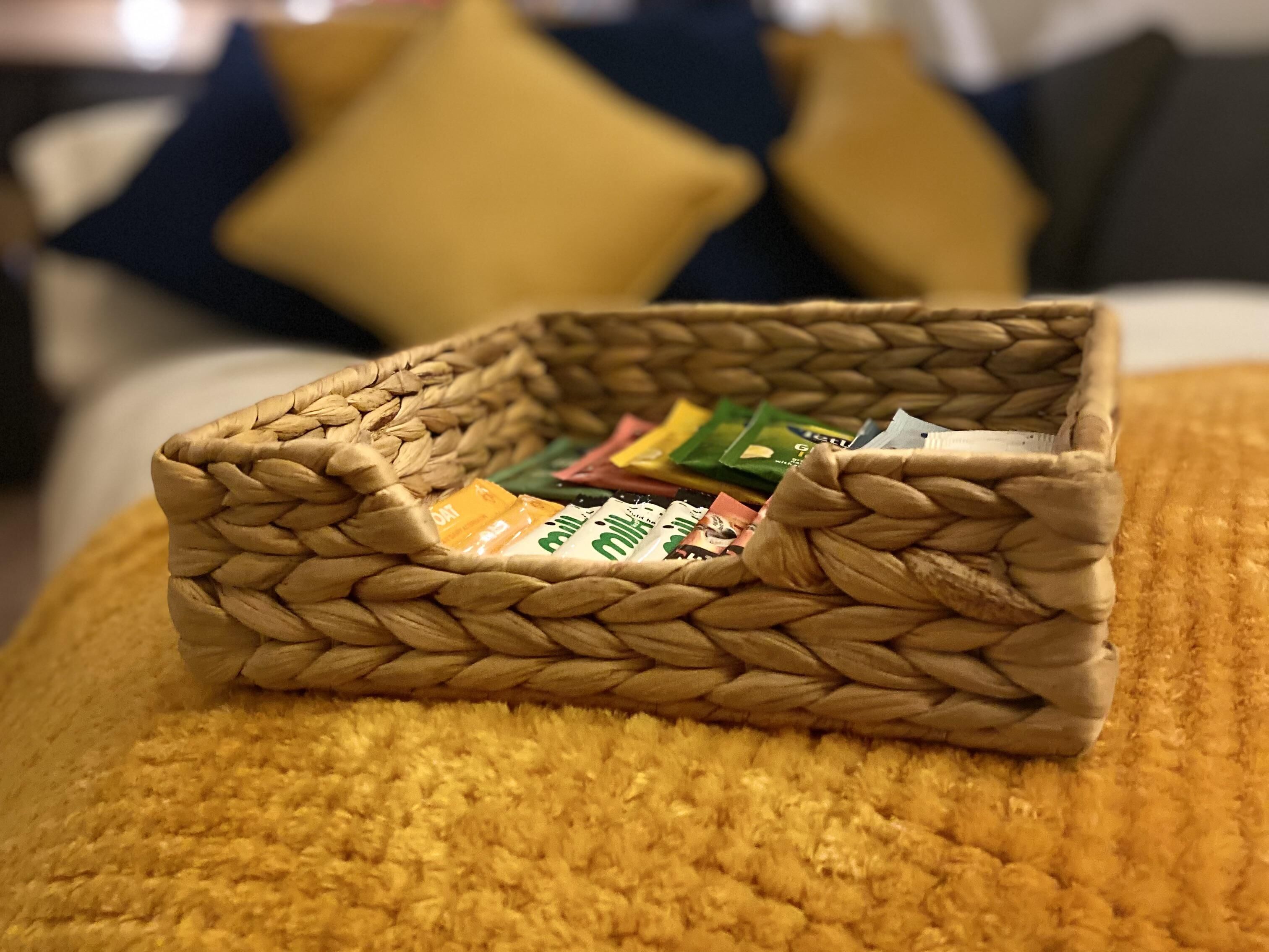 A woven basket filled with various snack packets on a yellow textured surface.
