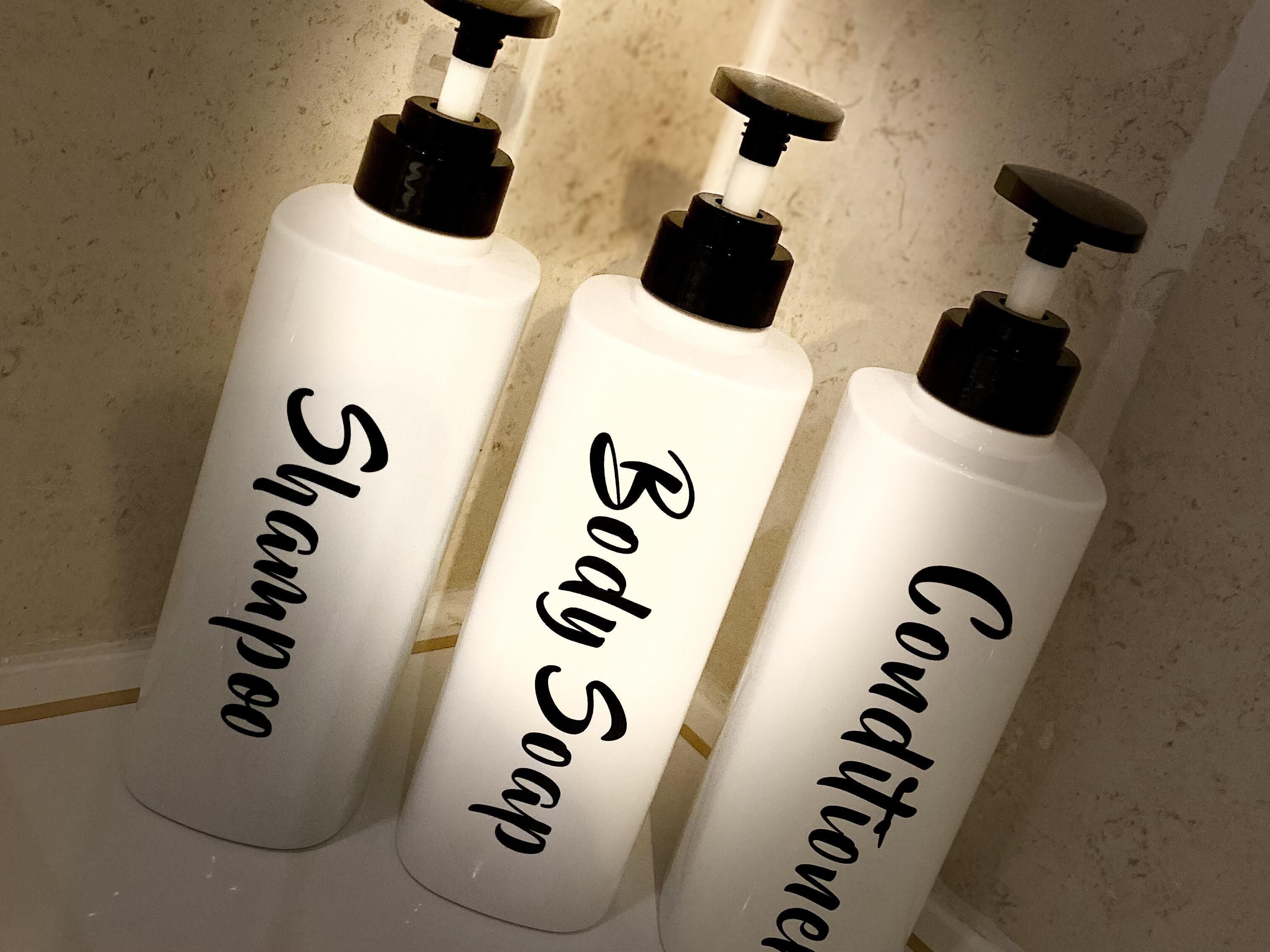 Three white bottles labeled 'Shampoo', 'Body Soap', and 'Conditioner' with black pumps.