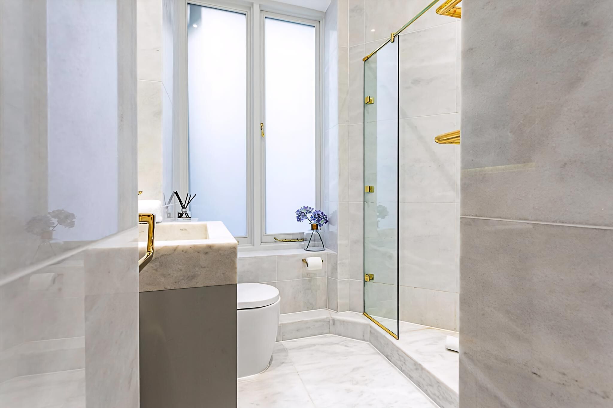 A modern bathroom with a glass shower enclosure, a marble sink, and a toilet.