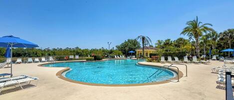 Ein Swimmingpool mit Liegestühlen und Sonnenschirmen, umgeben von Palmen und blauem Himmel.