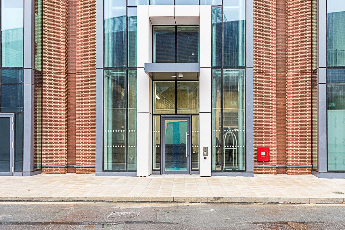 A modern building with a glass entrance, brick walls, and a tiled sidewalk.