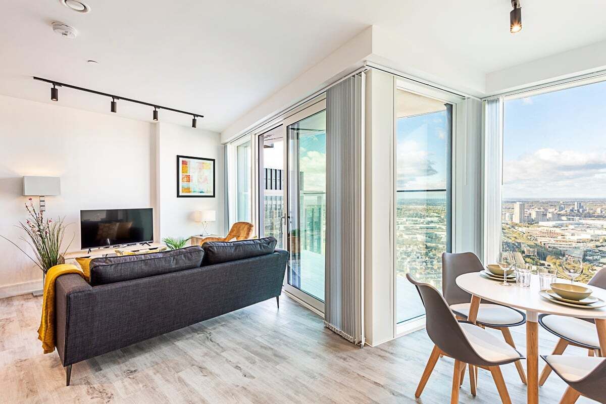 A modern living room with a sofa, TV, and dining area with a city view.