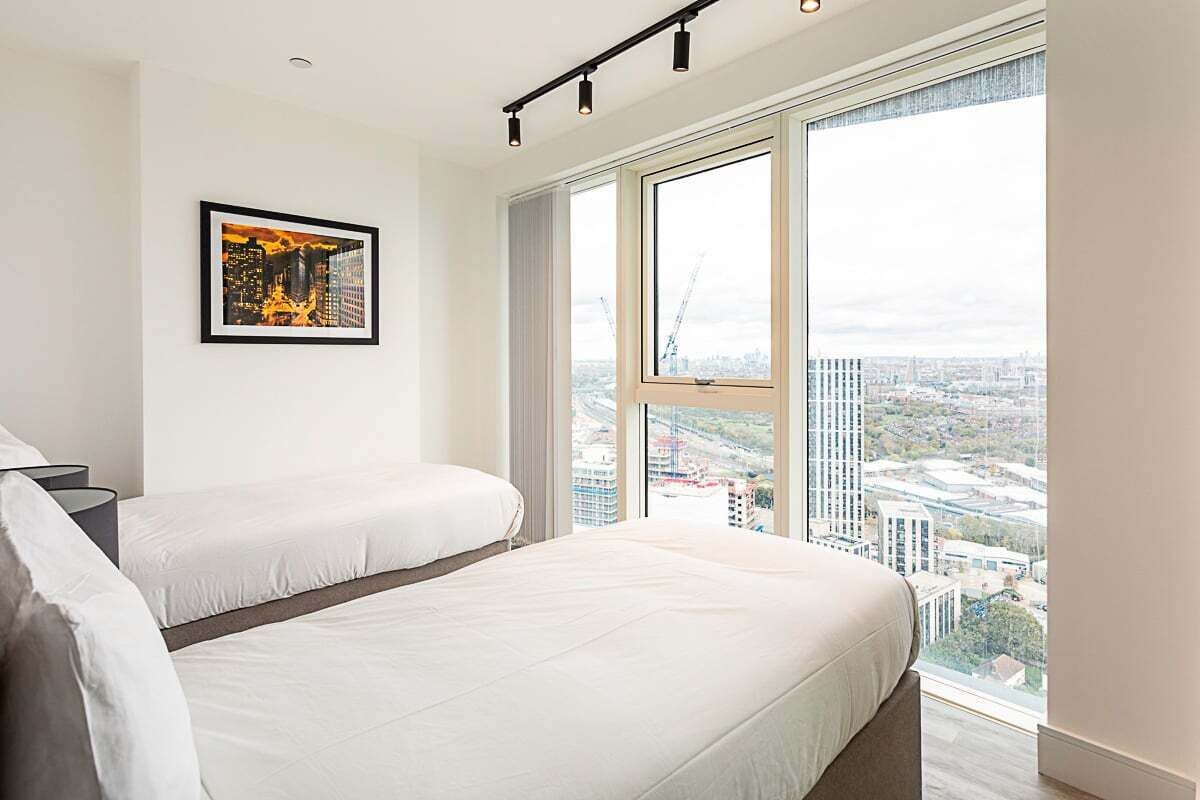 A modern hotel room with a large bed, a smaller bed, a city view, and a framed picture on the wall.
