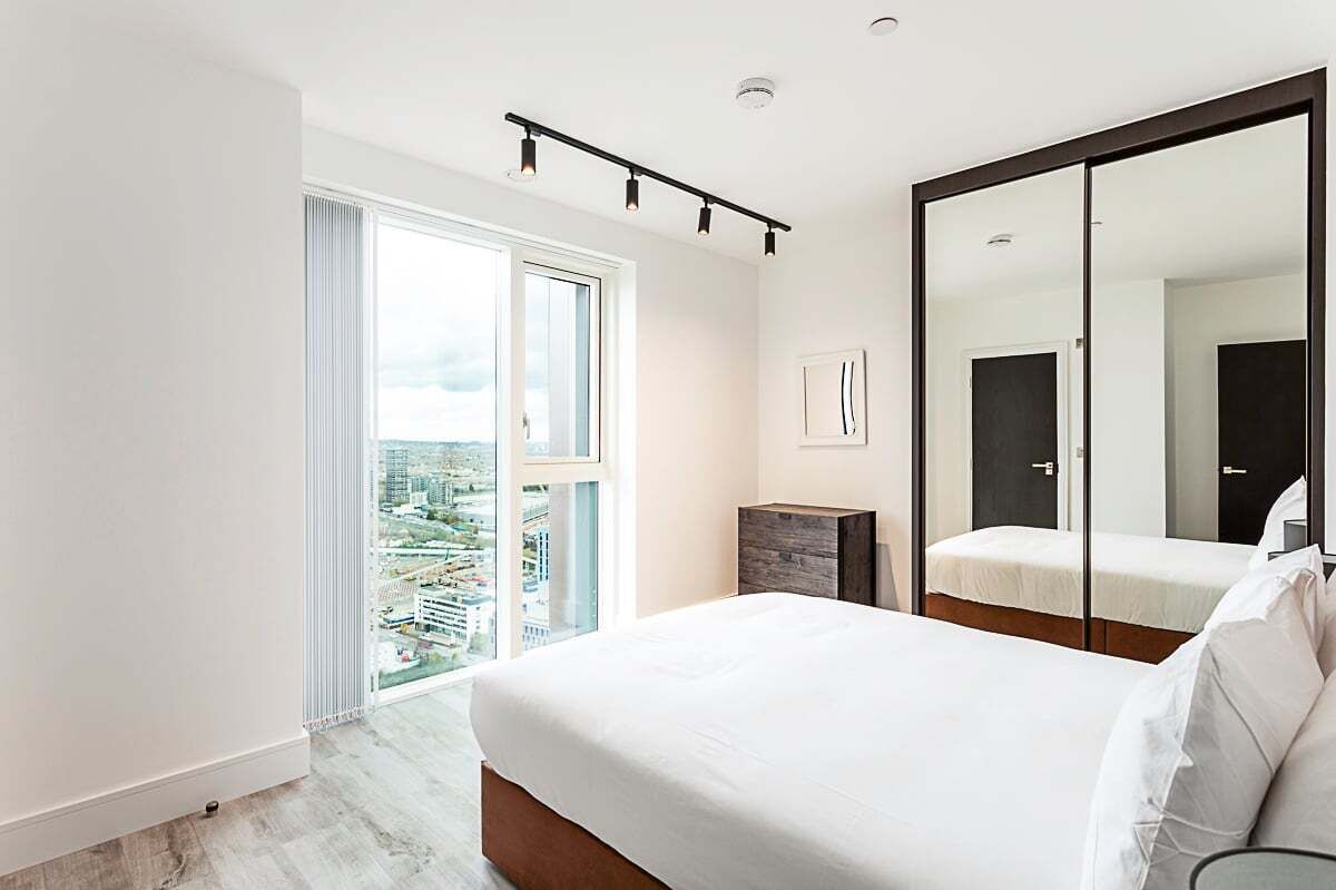 Un dormitorio moderno con una cama grande, un armario y un ventanal corredero que da a un balcón con vistas a la ciudad.