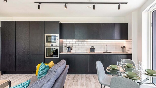 A modern kitchen with dark cabinetry, a built-in oven, and a tiled backsplash. - Icon Tower Flat III (London)
