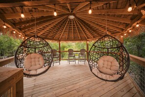 Ein hölzerner Pavillon mit einem Reetdach, Hängestühlen und einer Holzterrasse.