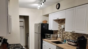 Una cocina moderna con armarios blancos, un refrigerador negro, horno integrado, microondas y un lavabo. Presenta una encimera de madera y un salpicadero con diseño de espiga.