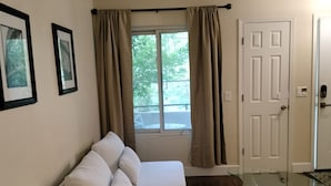 Una sala de estar moderna con un sofá blanco, una mesa de centro de vidrio y vistas a un balcón a través de una ventana con cortinas.