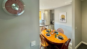 A dining area with a round wooden table set for four, surrounded by wooden chairs. A wall-mounted clock is visible on the left. - Waterloo House (Nottingham)