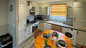 A compact kitchen with white cabinets, a built-in oven, and a window with orange blinds. - Waterloo House (Nottingham)