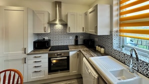 A modern kitchen with white cabinets, a stainless steel range hood, a built-in oven, and a dishwasher. - Waterloo House (Nottingham)
