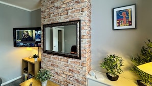 A living room with a brick fireplace, a mounted TV, a framed picture, and a small table with a plant. - Waterloo House (Nottingham)