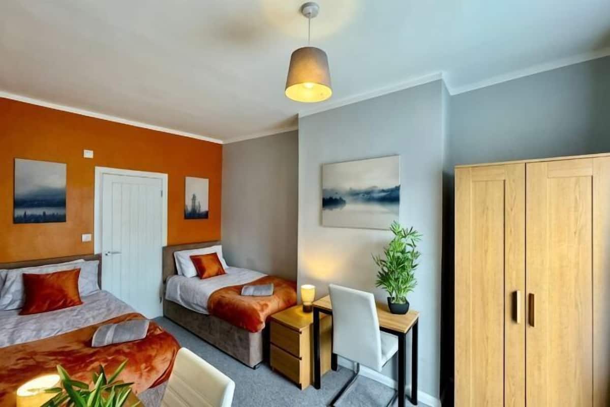 A bedroom with two beds, a desk, a chair, and a wardrobe.