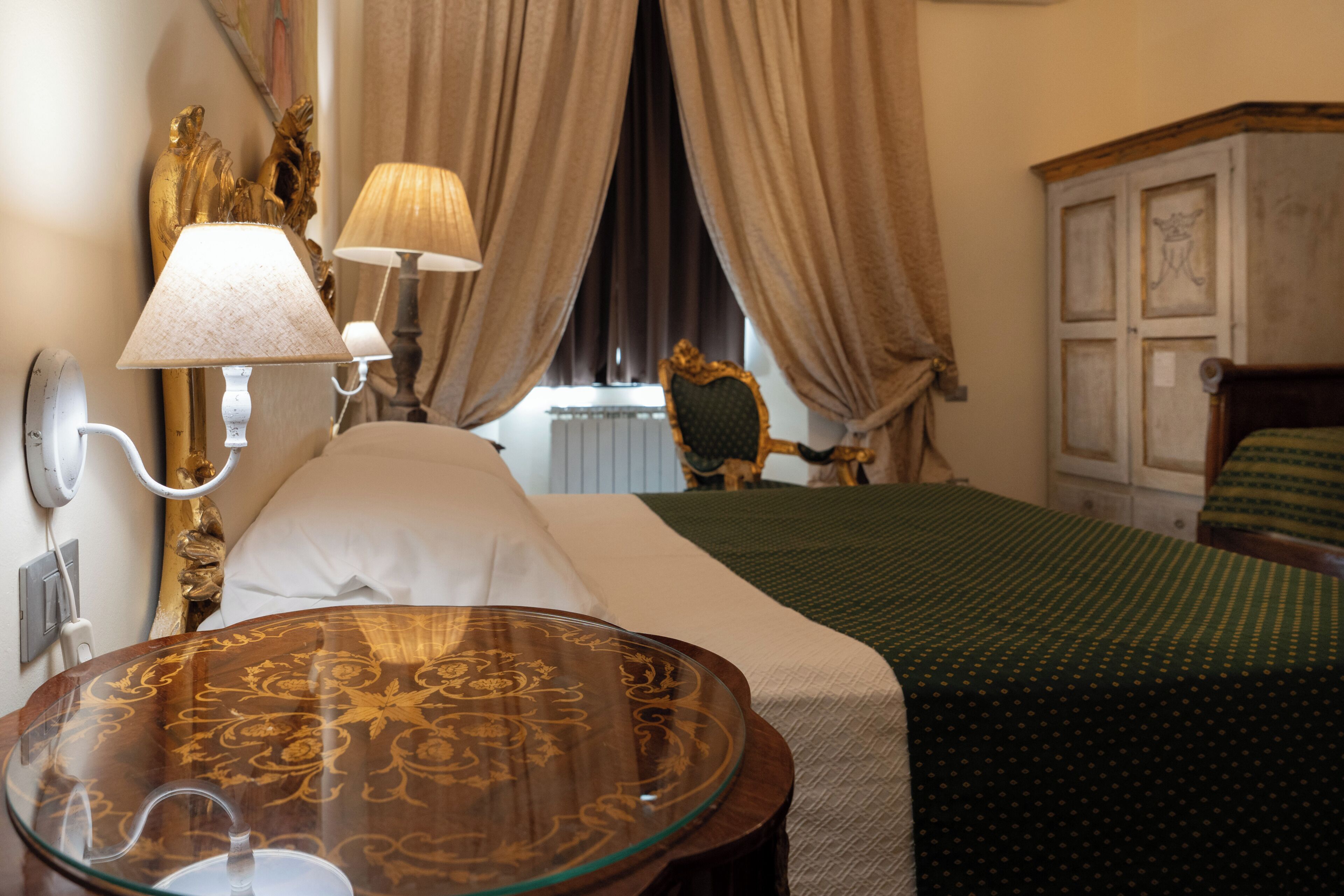 A hotel room with a bed, a glass table, a lamp, curtains, and a chair.