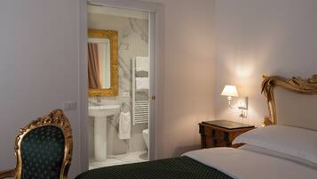 Ein Hotelzimmer mit Bett, Nachttisch mit Lampe, Stuhl, einem durchgegangene Tür sichtbaren Badezimmer und einer Marmorwand.