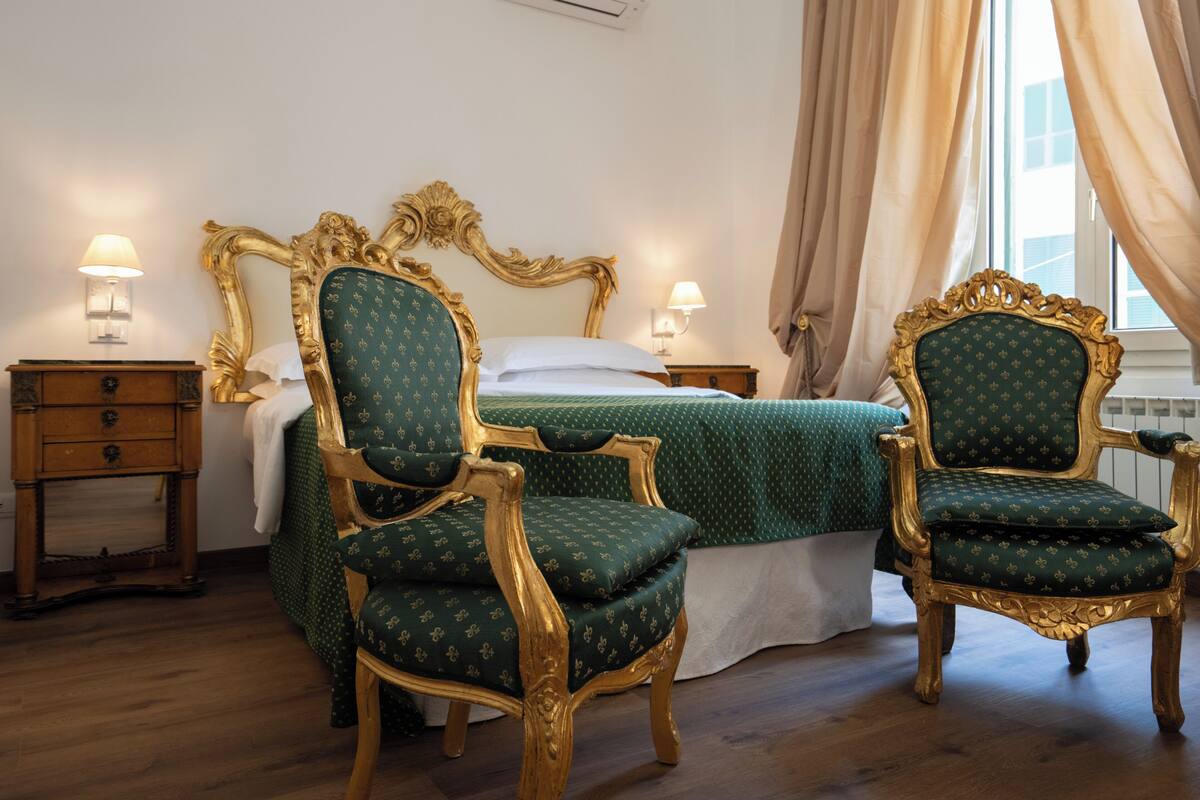 A room with a bed, two chairs, a nightstand, and a lamp.